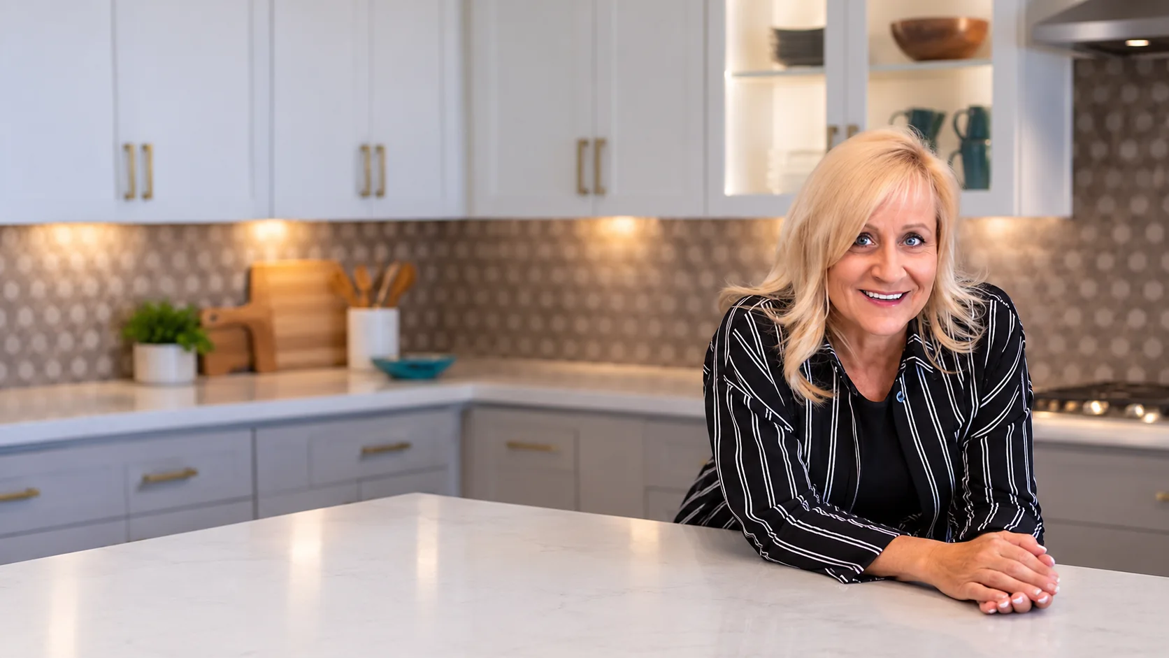Deah Hendriksz, a Sun City Grand Realtor, standing in a bright kitchen with a pool and desert mountains behind her